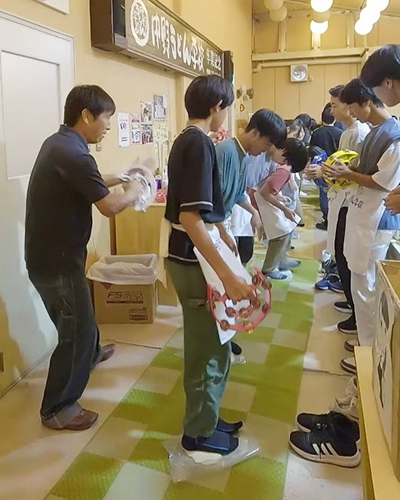 これが話題の「讃岐うどんづくり体験」！リズムに合わせてうどんを踏む生徒を、仲間たちがタンバリンや掛け声でにぎやかに盛り上げます。