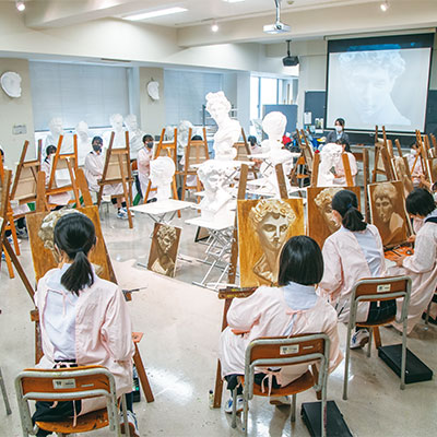 ピンクの作業着を着て油絵に取り組む生徒たち。講師の先生と、この日は教育実習生がサポートしました。