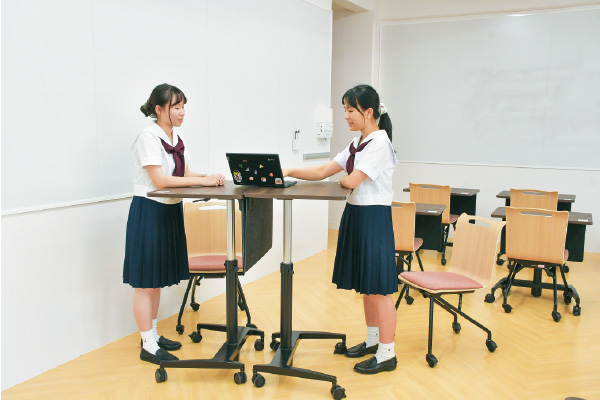 壁2面にホワイトボードを設置した「イングリッシュルーム」が2023年夏に完成。ハイテーブルにもなる机を導入したことで、「ペアワークやグループワークが多い英語の授業では、立ち話をしているフランクな感覚で、ディスカッションがより活発化します」（飯川先生）