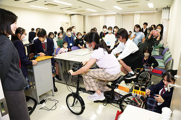 小学生が自転車発電装置をこいで発電し、テレビの電源を入れる実験を行いました。