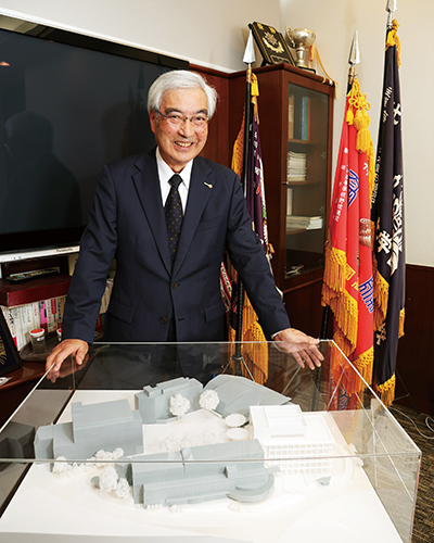 完成予定模型を使って新校舎のコンセプトを説明をする小塚良雄理事長