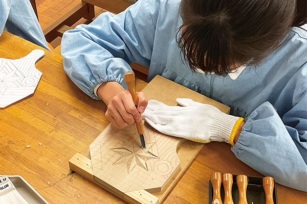 中1「美術」の鍋敷き制作。彫刻刀を使って片面に模様を彫刻し、自宅で使えるように仕上げます。