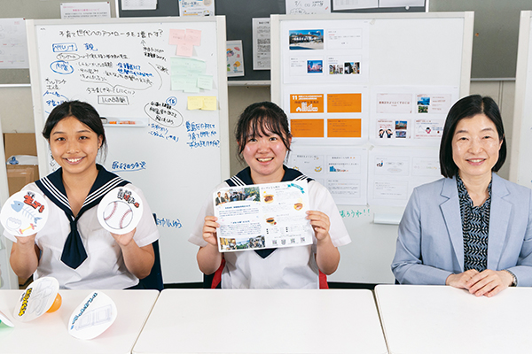 『地域貢献メッセ』のブースで使ったガチャガチャゴミを手にするY・Kさん（左）、『巣鴨駅前商店街活性化プロジェクト』の企画案を手にしたT・Yさん（中）、飯島先生（右）。