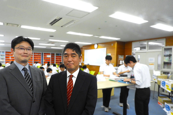 高橋先生（左）と大重先生（右）。放課後から20時まで利用できる高3専用自習室「進学センター」にて。あえて仕切りを設けず、仲間が学ぶ姿を感じながら集中できる空間です。校長先生がホワイトボードに出題する数学の問題も、進学センターの名物となっています。