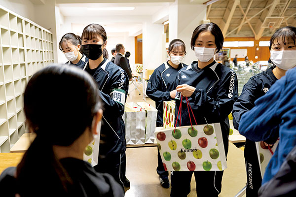 説明会会場の入口では、バレーボール部の生徒が受付を担当。資料が入った手提げバッグを明るくていねいに手渡していた。袋を彩る鮮やかな色彩のリンゴの絵は、美術の時間に生徒が描いたもの。